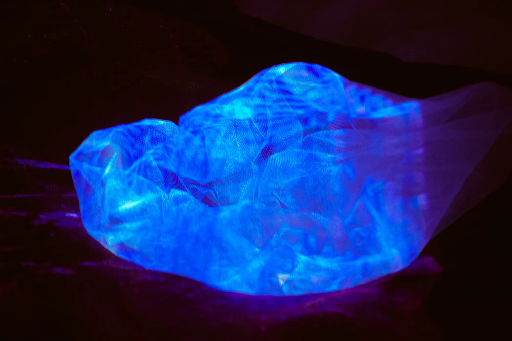Membrana escultórica translúcida iluminada por projeções azuis e violetas